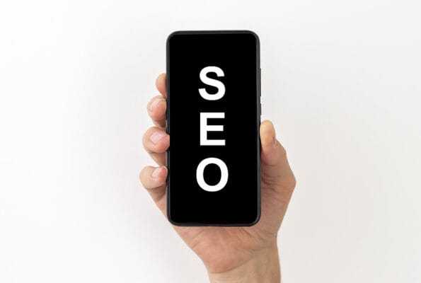 SEO search engine optimization word acronym inscription on a black screen of a mobile phone in a male hand isolated on a white background. SEO concept.