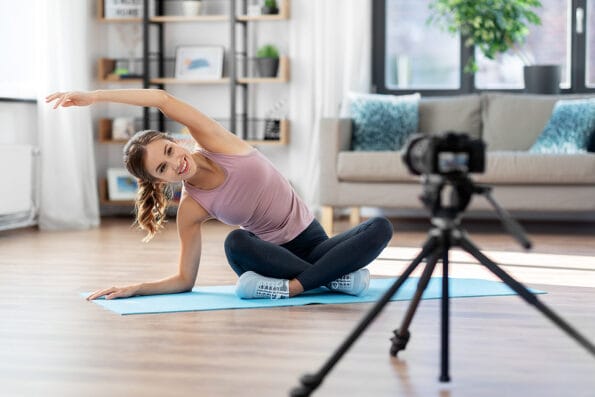 side hustle fitness, sport and video blogging concept - woman or blogger with camera streaming online yoga class at home