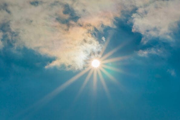 The sun in the blue sky under the clouds. Sunny day. Blue sky. Bright midday sun illuminates the space. Blue sky with clouds and sun reflection. The sun shines bright in the daytime in summer.