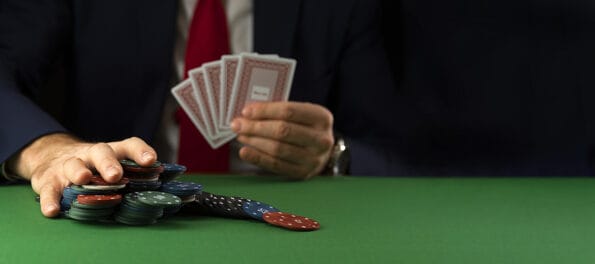Businessman at green playing table with gambling chips and cards playing poker and blackjack in casino.