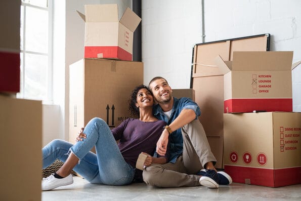 Young couple resting after moving into a new home and daydreaming. Multiethnic contemplative couple sitting on floor and thinking  while looking up. Happy couple buy new apartment and plan a family.