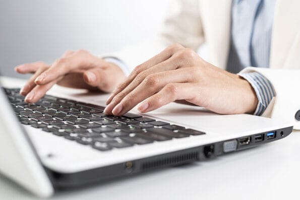 Man in business suit sitting at desk and working at laptop computer. Close-up of male hands typing on laptop keyboard. Businessman at workplace in office. Business innovation and digital technology