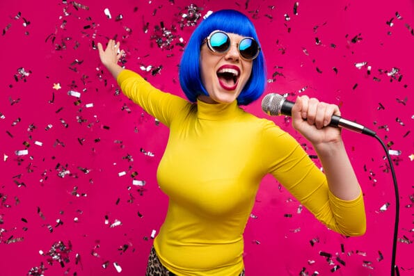 Closeup photo of funny nice lady singer party night club microphone karaoke confetti falling wear specs yellow turtleneck blue wig isolated bright pink color background