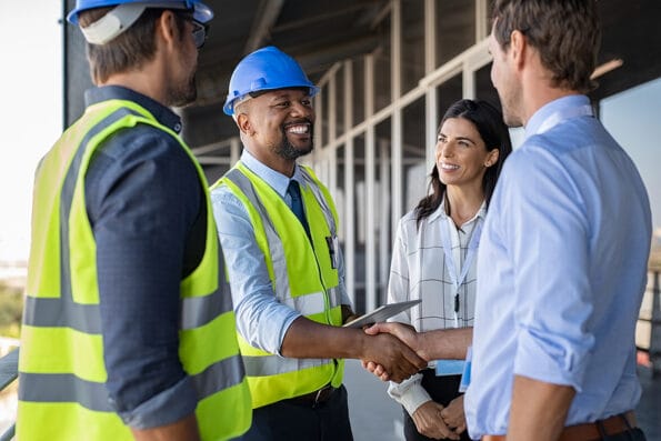 Smiling engineer shaking hands at construction site with happy architect. Handshake between african construction manager with businessman at bulding site. Team of workers conclude an agreement.
