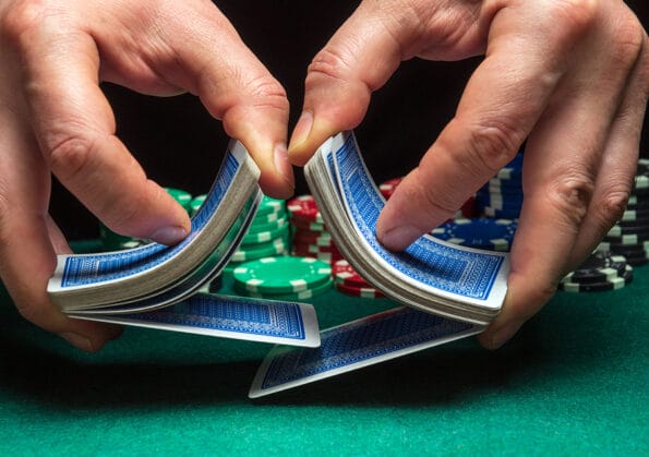 Close-up hands of a person-dealer or croupier shuffling poker cards in a poker club on the background of a table, chips. Poker game or gaming business concept
