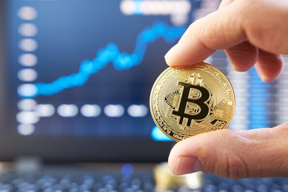 bitcoin Male hand showing gold bitcoin. laptop keyboard with basic candlestick green red graph price in background. Worldwide cryptocurrency and digital payment concepts. Bitcoin price rises