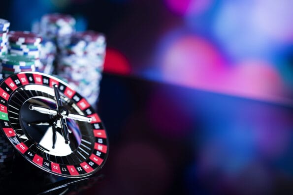 Casino gambling theme. High contrast image of casino roulette and poker chips on a gaming table, all on colorful bokeh background. Place for typography and logo.