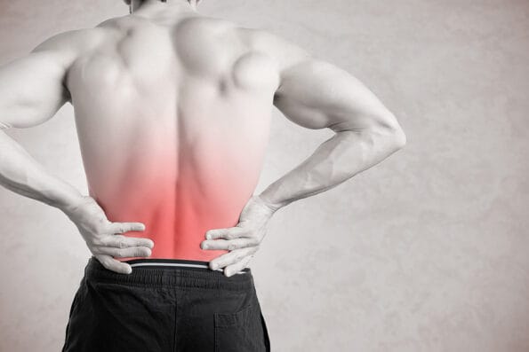 Male athlete with pain in his lower back isolated in grey. Red spot around muscle soreness.