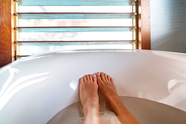 Bathtub pillow feet soaking in warm water woman taking a warm bath at luxury bathroom villa. Window view.