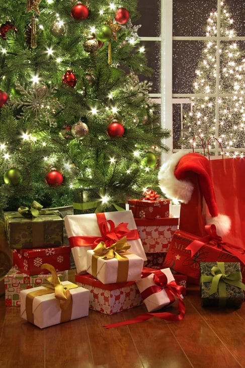 Brightly lit christmas tree with lots of gifts near window