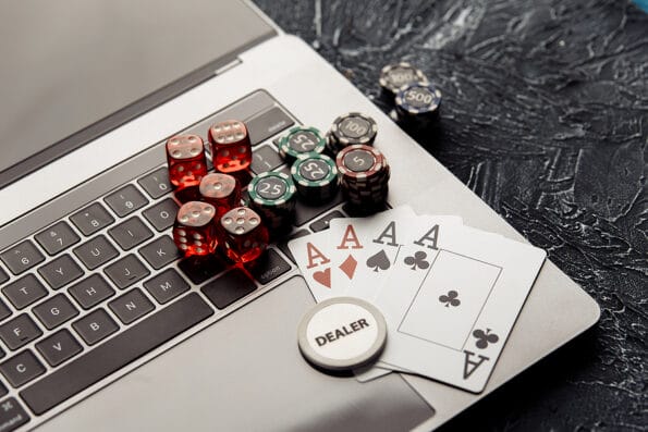 Online Gaming Chips, red dices and playing cards on laptop for poker online or casino gambling close-up. Online casino concept