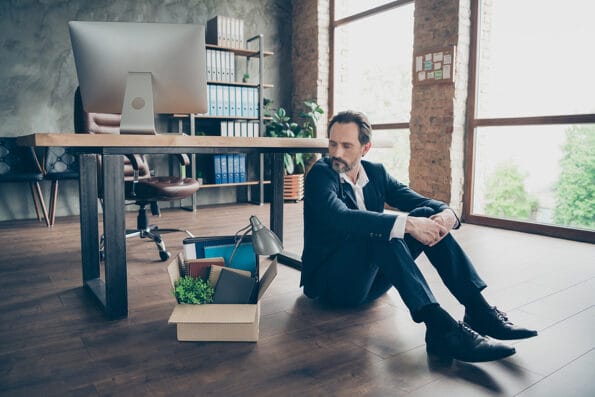 Photo of laid off dismissed sad worker mature guy fail fired agent loser lost job packed belongings look thoughtful box financial crisis sit floor wooden parquet workstation office indoors termination