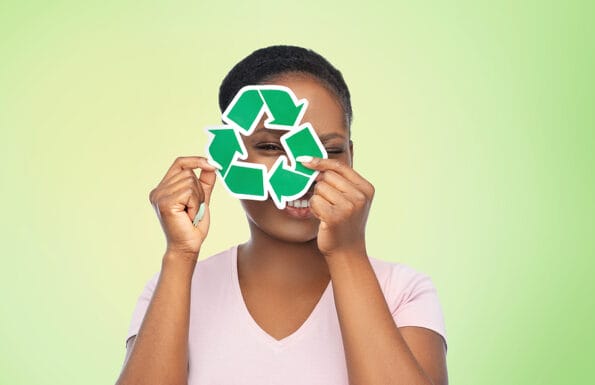 eco living, environment and sustainability concept - portrait of happy smiling young african american woman looking through recycling sign over green background
