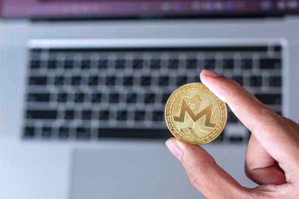 businessman hand hold golden Monero (XMR) cryptocurrency coin over keyboard laptop, Monero coin. Crypto is Digital Money within the blockchain network