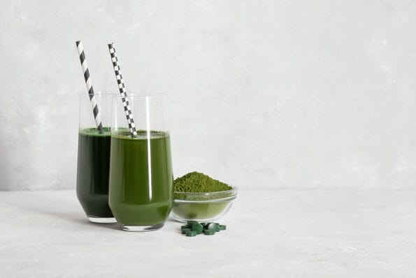 Chlorella and spirulina green detox drinks. Chlorella powder and spirulina tablets, glasses with green drinks on a gray background. Superfood concept. Copy space.