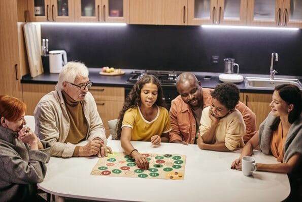 Multiethnic big family sitting at the table in the kitchen and playing board game together in team