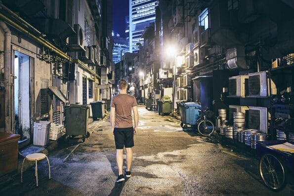 Young man walking throught dark narrow street against skyscrapers of the city, Singapore
