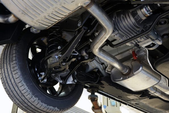 A modern car in a car service on a lift. Bottom view of the car. Details and structure of the suspension, elements of the exhaust system are visible. Car service and auto parts. Selected focus.