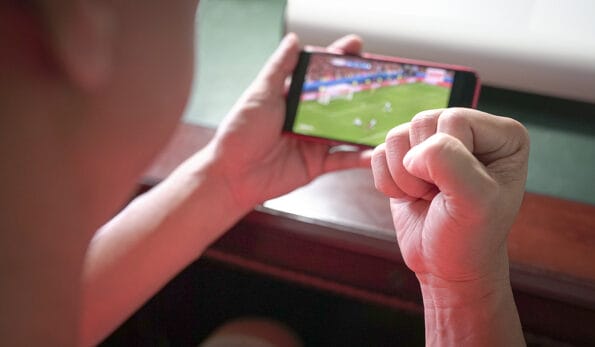Sports fan with fist up in celebration while watching sports streaming on mobile phone. Close up view.