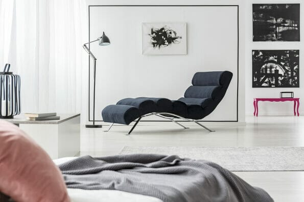 Black chaise lounge lamp, art gallery and bed with a pink pillow in elegant bedroom interior