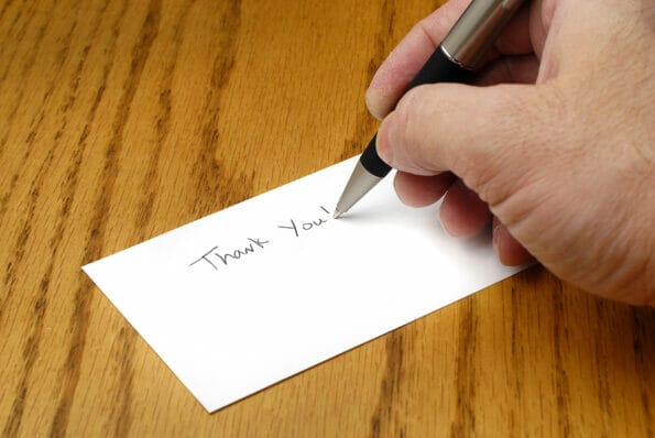 Person writing thank you note with pen on card