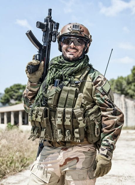 Army soldier, special forces infantryman, Navy SEALs fighter in camouflage uniform, combat helmet and plate carrier, armed submachine gun. Half-length portrait of happy smiling commando shooter