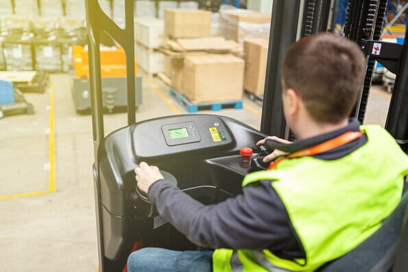 Storehouse employee in uniform working on forklift in modern automatic warehouse. Boxes are on the shelves of the warehouse. Warehousing, machinery concept. Logistics in stock.