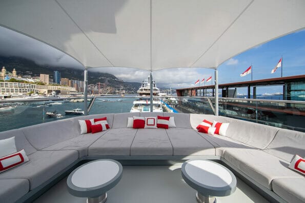 The front deck of huge yacht in port of Monaco at sunny day, landmarks of Monte-Carlo and a lot of motorboats are on background, the lounge zone for a chilling, mega yacht is moored in marina
