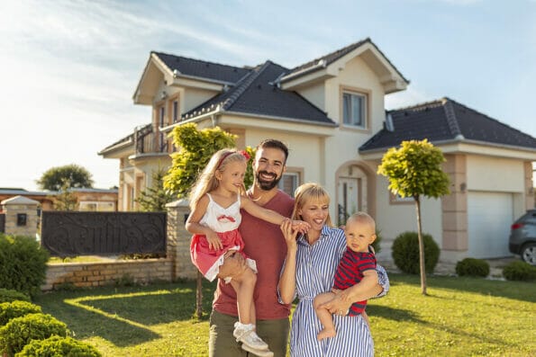 Family buying a new house; parents and children hugging and having fun standing in front of their new house; real estate market and property sales concept