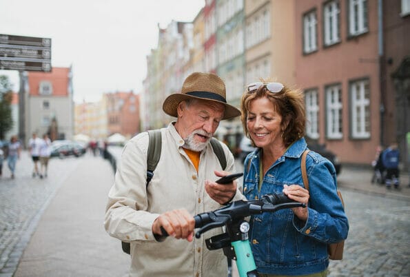 Portrait of happy senior couple tourists riding scooter together outdoors in town