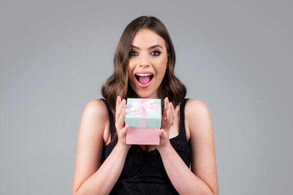 Excited woman with present gift box posing with surprised face expression, isolated background. Christmas, valentines or birthday gifts. Beauty portrait of beautiful female model.
