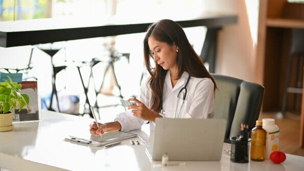 Asian female doctor or dentist reading a medical research paper or past medical history papers in the hospital office. doctor office workspace concept