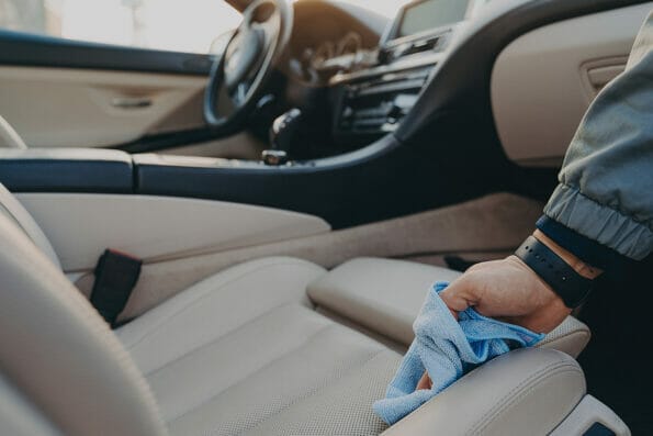 Cropped shot of man cleaning car interior, wiping fabric passenger seat with microfiber cloth, removing dirt and dust in modern vehicle salon with rag. Car wash concept